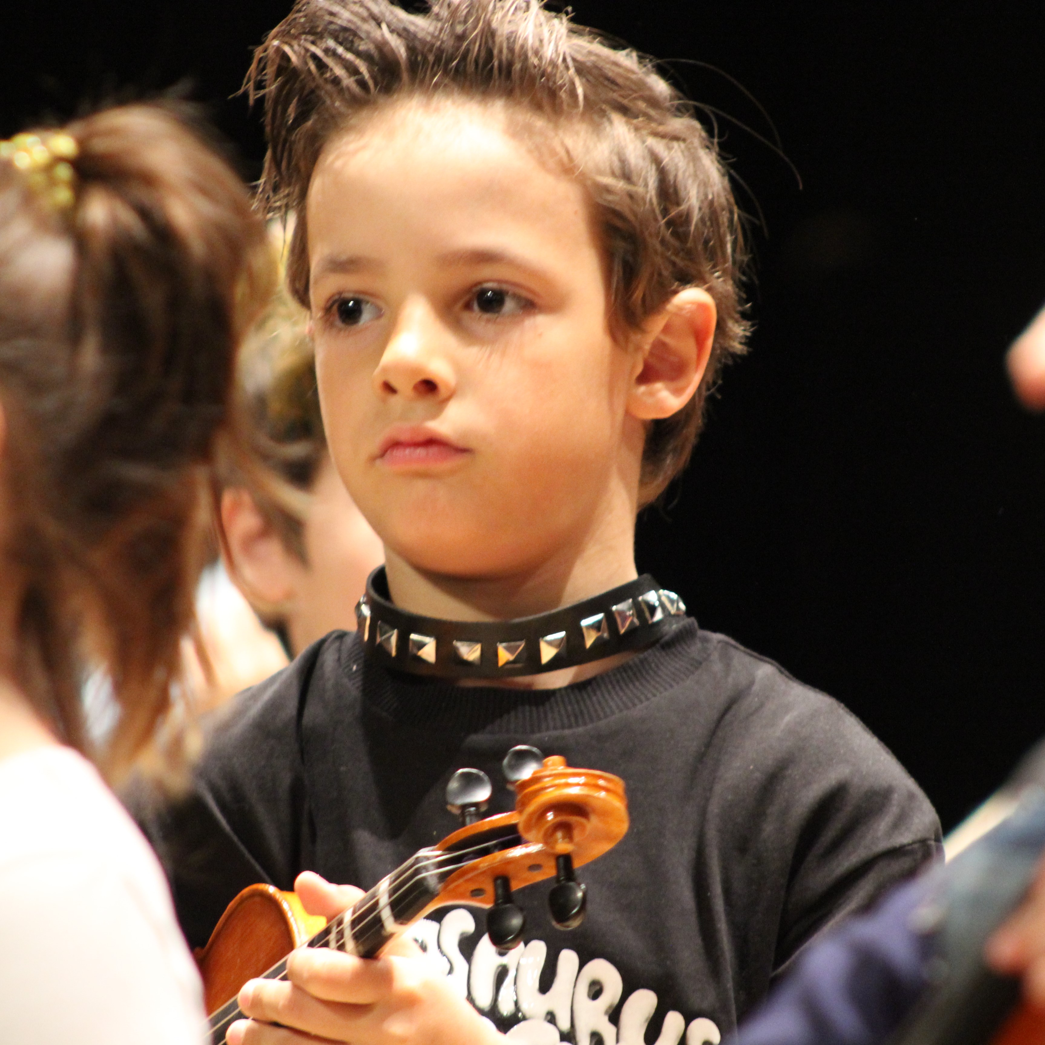 Alumno de violín de ocho esperando a que llegue el turno de su melodía en la pieza que está sonando en el ensayo para el concierto