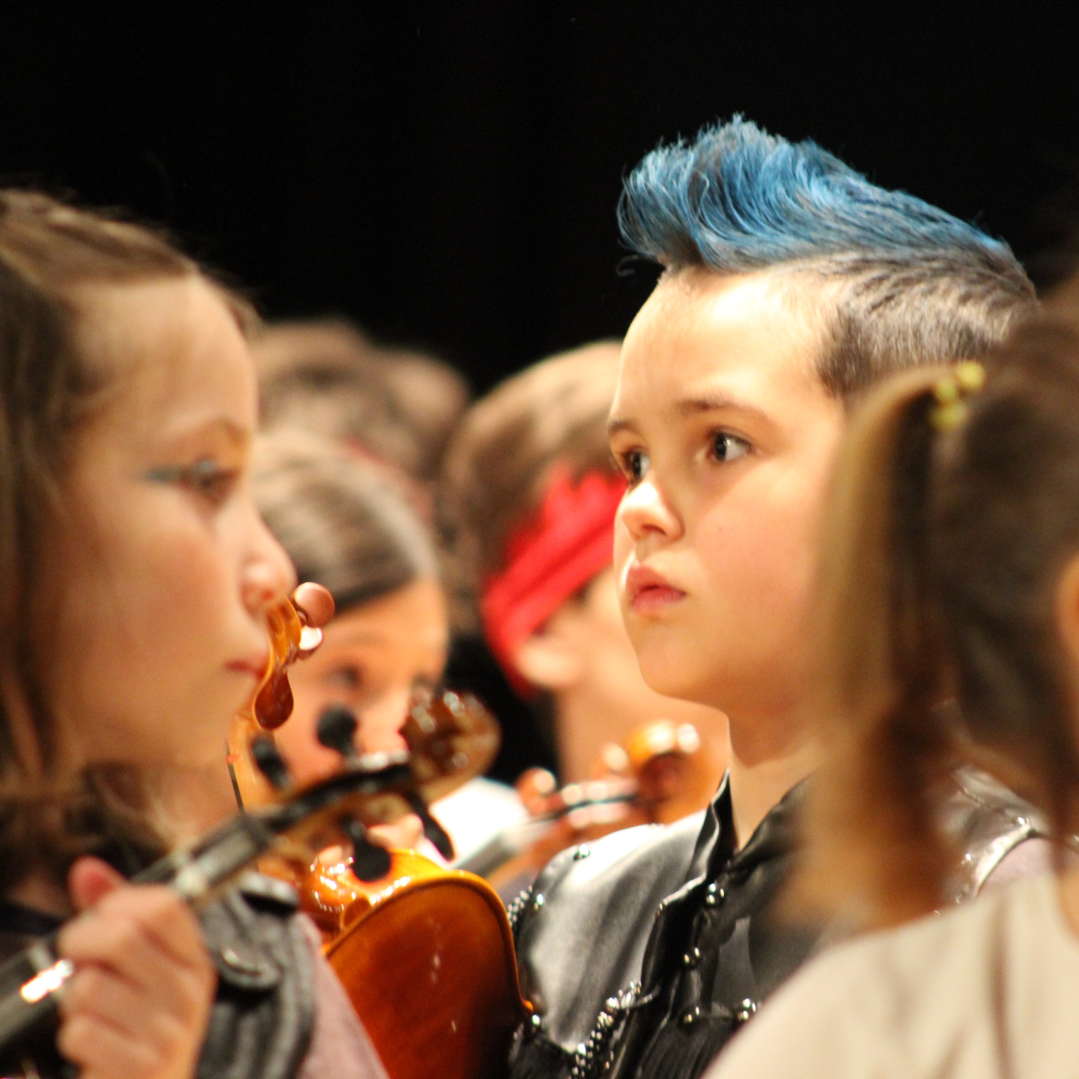 Alumno de violín en posición de descanso y muy concentrado a punto de comenzar su concierto disfrazado de concierto con una cresta azul impresionante