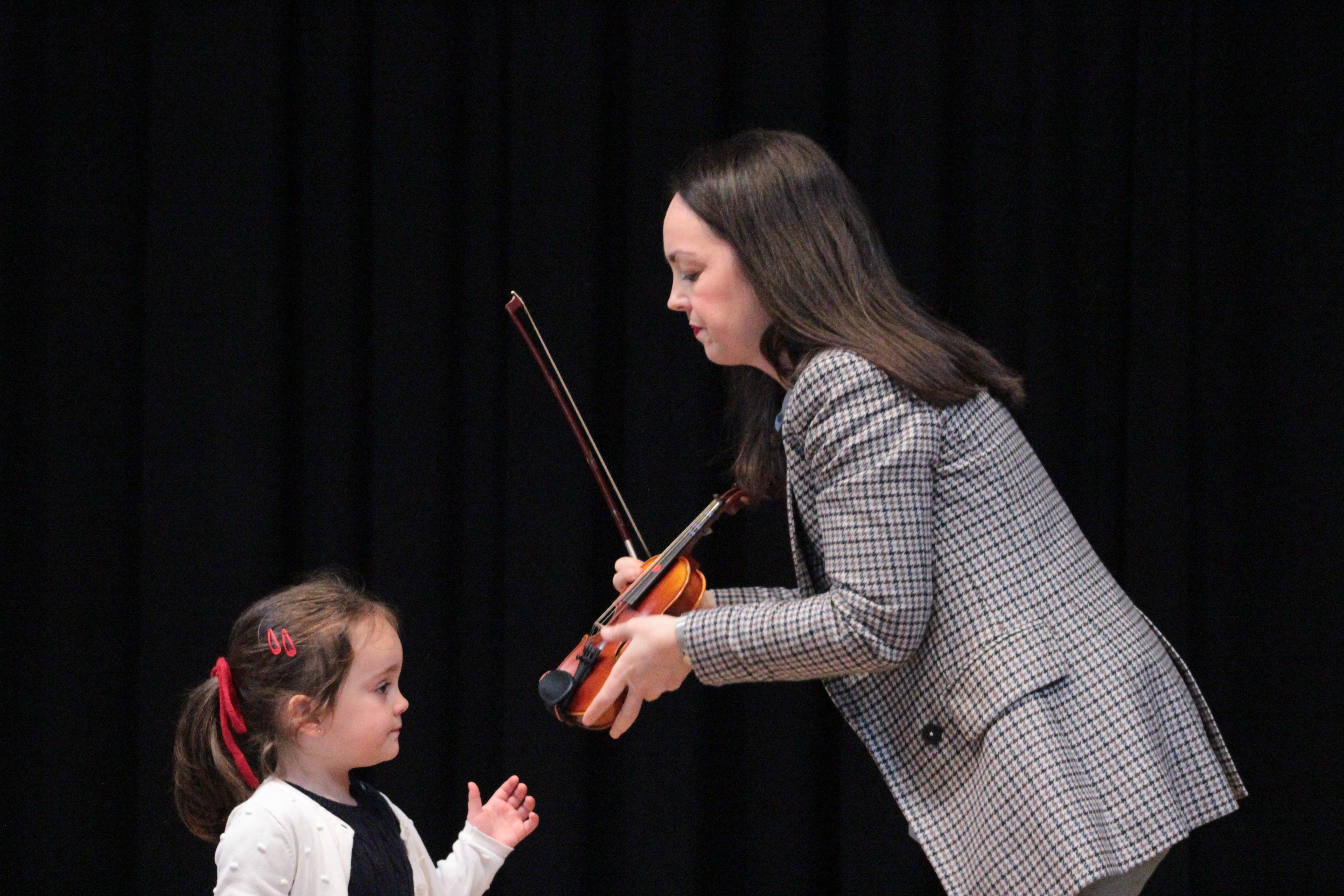 Profesora ayudando a una alumna muy pequeña a colocar correctamente el violín sobre el hombro.