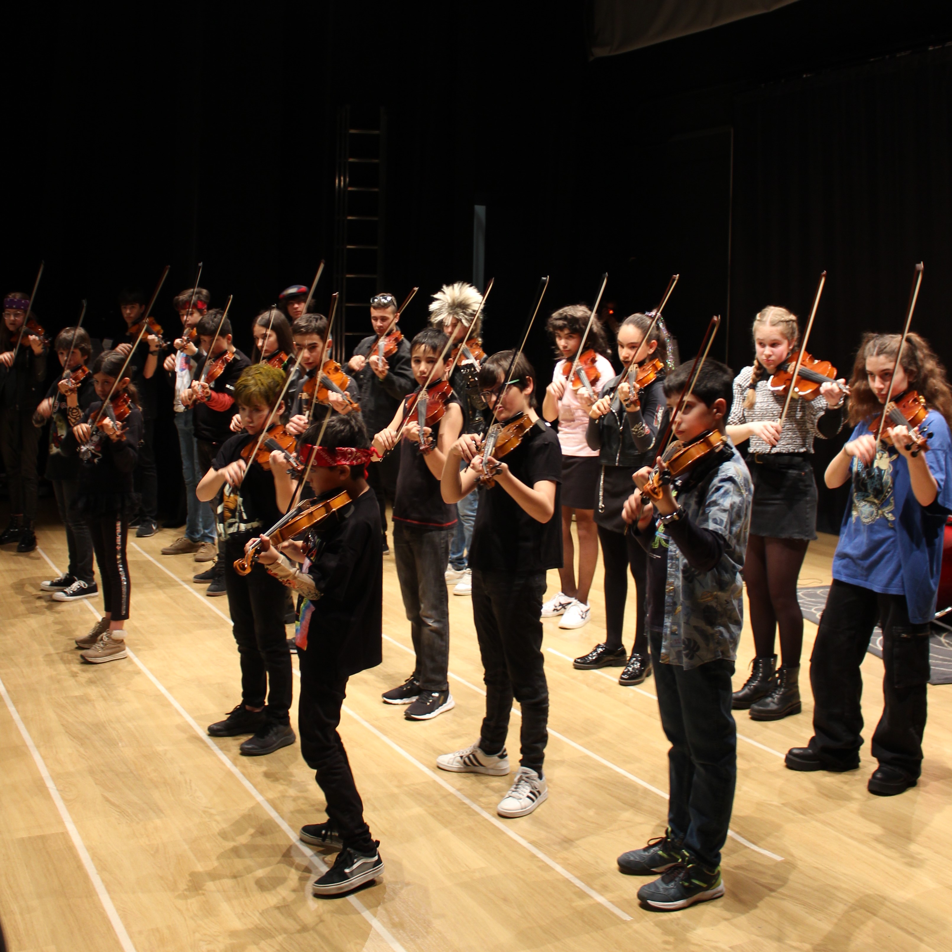 Veinte alumnos de violín participando tocando juntos música moderna con todos sus arcos acompasados
